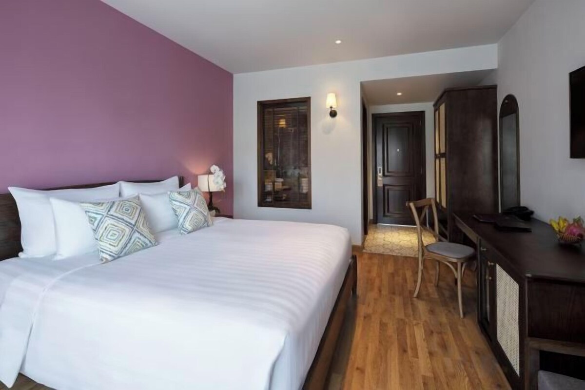 Une chambre d’hôtel avec un grand lit, un bureau et une chaise. Une porte donne accès à une autre pièce.