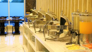 Un buffet composé de plusieurs plats de service en acier inoxydable, maintenus au chaud, et d’un distributeur de jus.