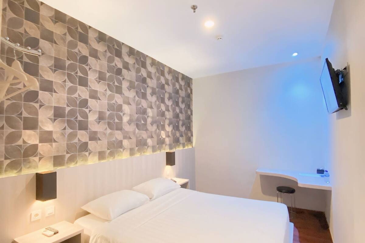Una habitación de hotel moderna con una cama grande, un escritorio y un televisor de pantalla plana montado en la pared.