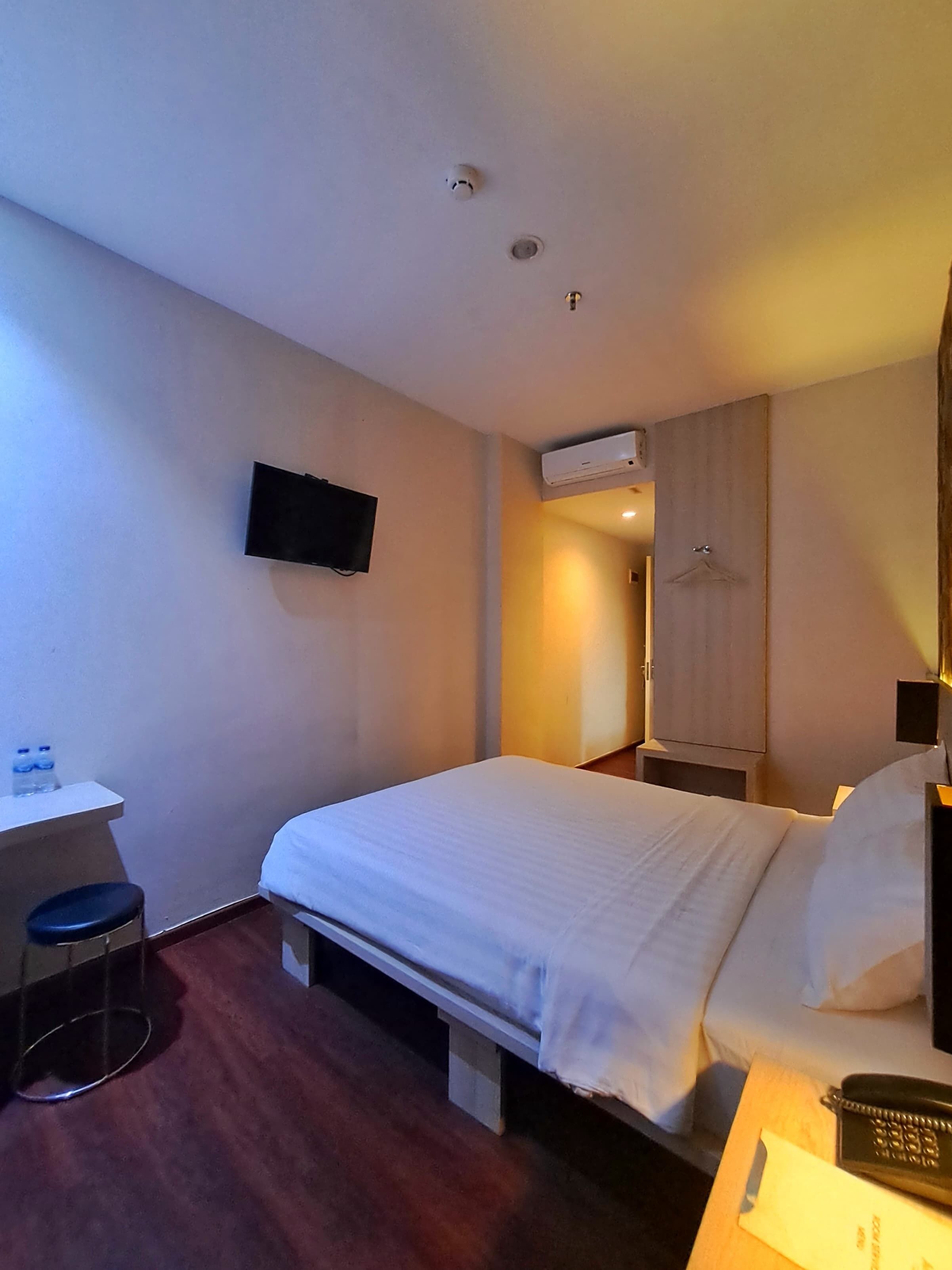 Ein Hotelzimmer mit Bett, Schreibtisch mit Stuhl, Fernseher, Klimaanlage und Kleiderschrank.