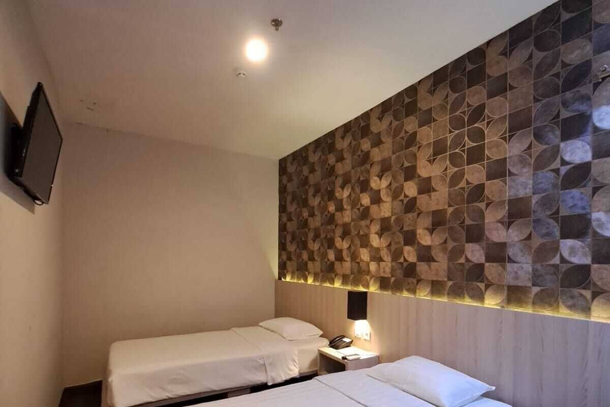 Una habitación de hotel con dos camas individuales, un televisor instalado en la pared y un panel decorativo.