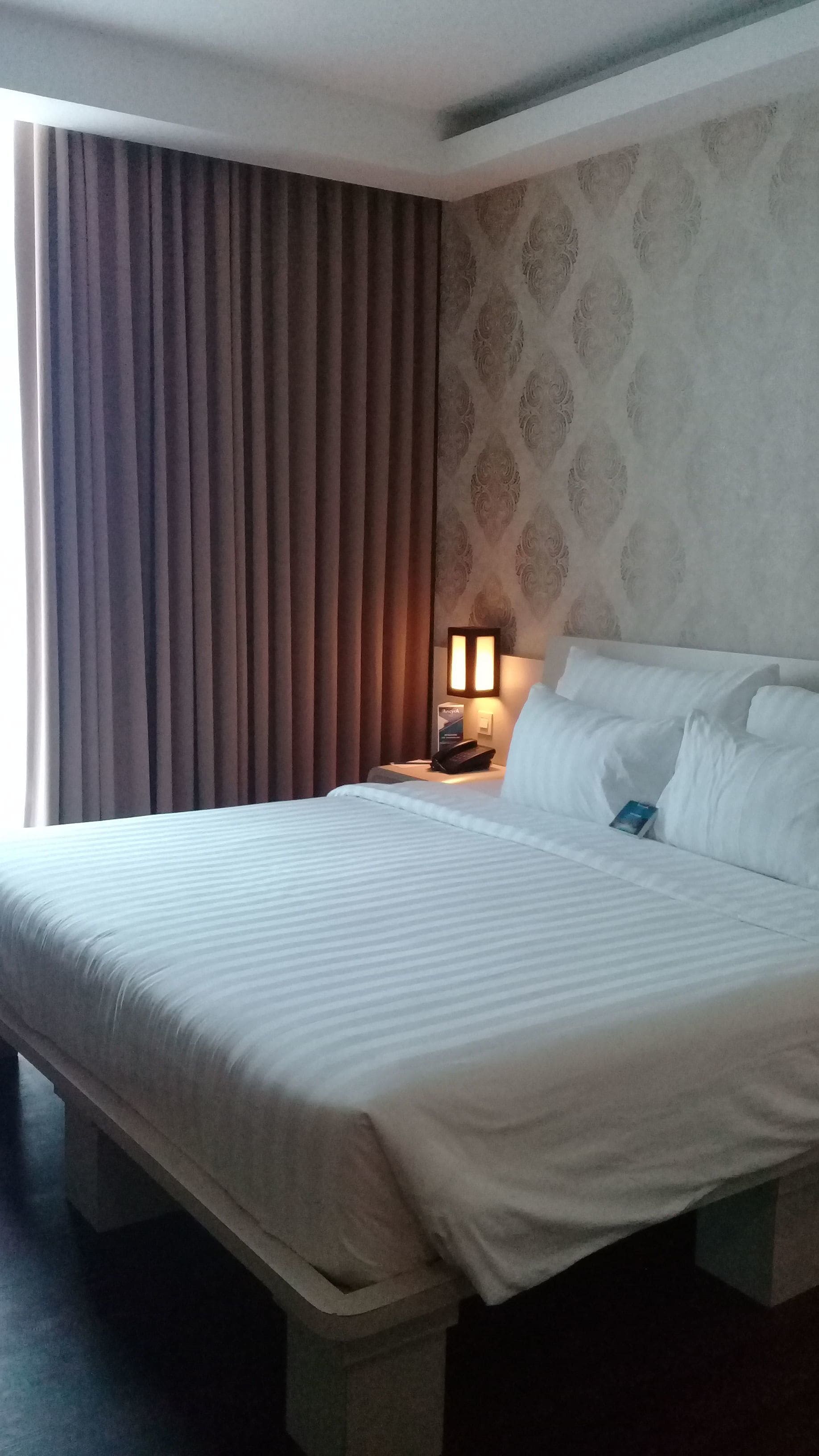 Ein Hotelzimmer mit einem großen Bett, einem Nachttisch mit Lampe und einer Wand mit Muster.