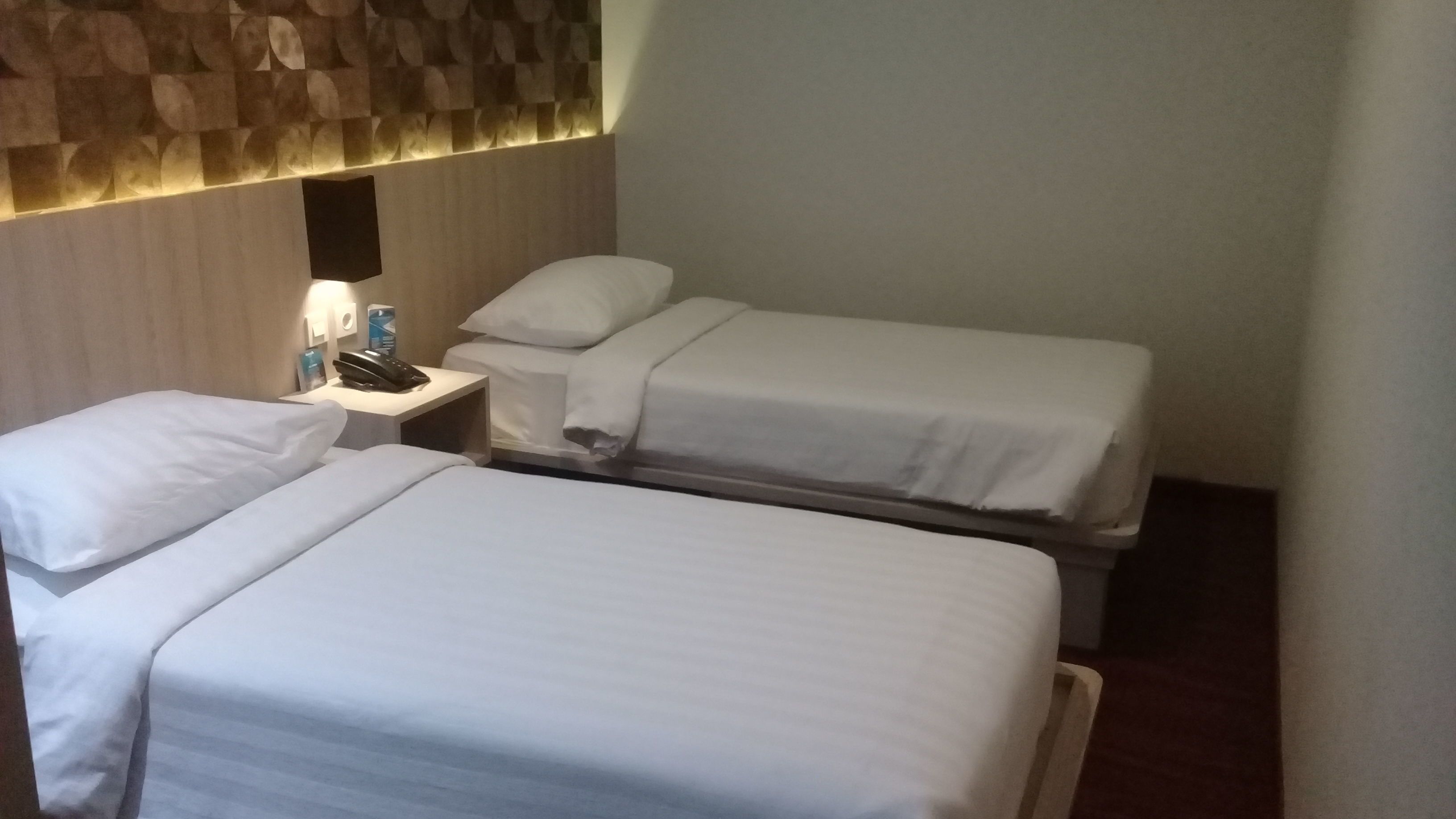 A hotel room with two single beds, a bedside table with a phone and a bottle, and a wall with a textured pattern.
