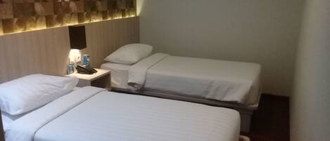 A hotel room with two single beds, a bedside table with a phone and a bottle, and a wall with a textured pattern.