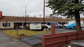 A motel with a 'WELCOME FRIENDLY' sign, a parking lot with several cars, and a red picket fence. - Modoc Inn (Alturas)