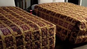 A hotel room with two beds, each with a patterned bedspread, a bedside lamp, and a nightstand. - Modoc Inn (Alturas)