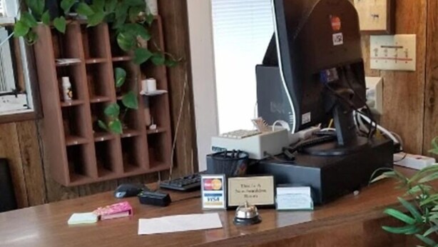 A wooden reception desk with a computer monitor, a plant, and a small shelf with various items. - Modoc Inn (Alturas)