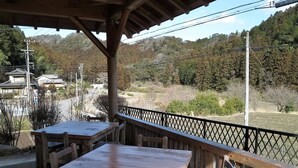 A wooden outdoor seating area with tables and benches, overlooking a hilly landscape with trees and power lines. - Minshuku Ryokan Kawai (Shinshiro)