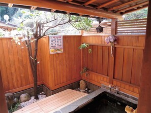 A traditional Japanese onsen with wooden walls, a stone platform, and a small pond. - Minshuku Ryokan Kawai (Shinshiro)
