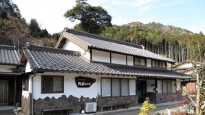 A traditional Japanese building with a tiled roof and a stone wall. There is a sign with Japanese characters and a bench outside. - Minshuku Ryokan Kawai (Shinshiro)