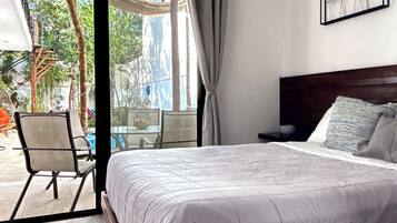 A bedroom with a bed, a chair, a table, and a view of the outdoors.