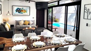 A dining area with a wooden table set for six, surrounded by white chairs.