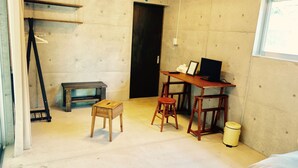 A room with a wooden desk, two stools, a small wooden table, a trash bin, and a door. - Retya (Ishigaki)