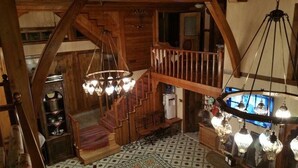 A wooden interior with a staircase, chandeliers, and a patterned floor.