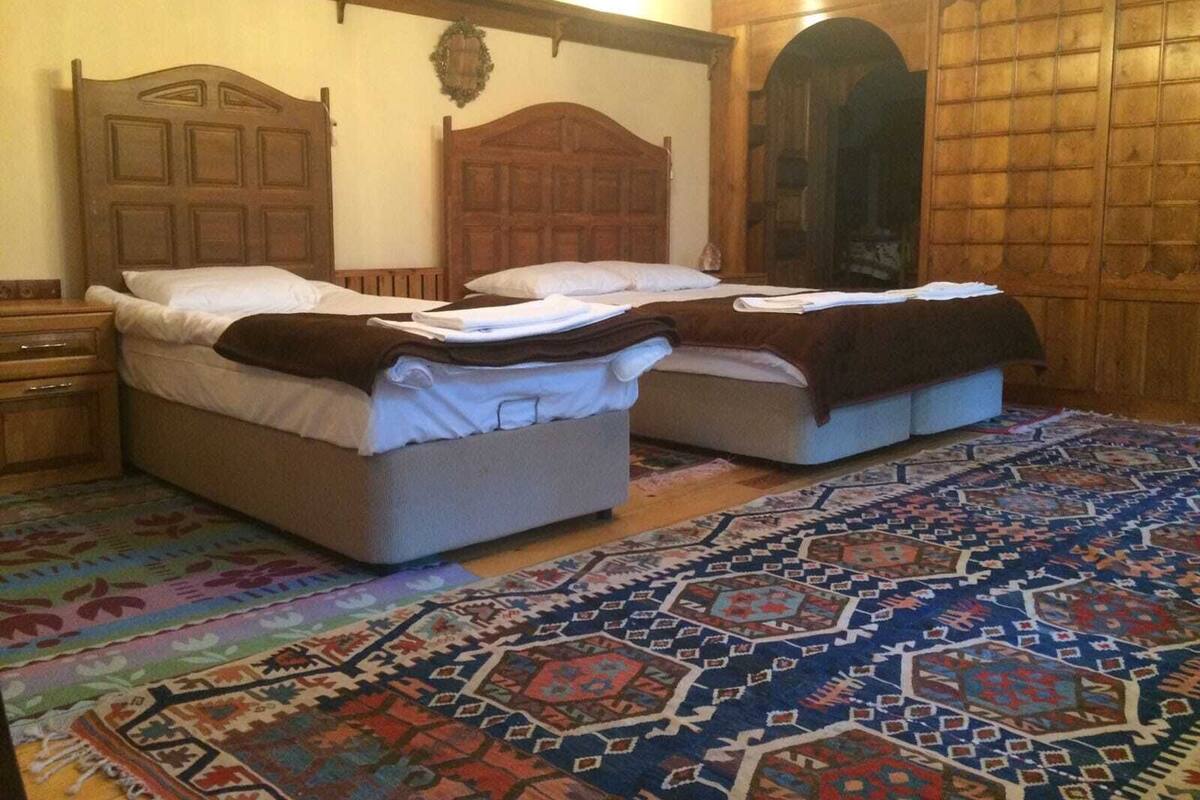 A room with two beds, wooden headboards, a patterned rug, and a wooden wardrobe.