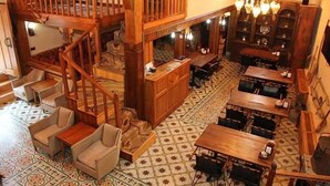 A spacious hotel lobby with a wooden staircase, multiple seating areas, and patterned floor tiles.