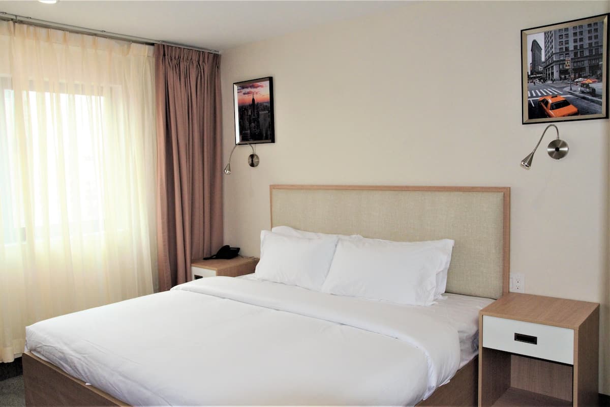 A hotel room with a large bed, a nightstand, a drawer, a wall-mounted phone, and two framed pictures.