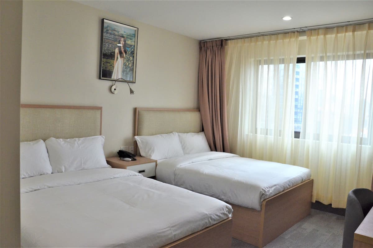 A hotel room with two single beds, a nightstand, a desk, and a window with curtains.