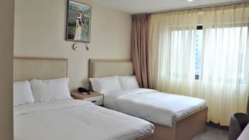 Une chambre d’hôtel avec deux lits simples, une table de chevet, un bureau et une fenêtre avec des rideaux.