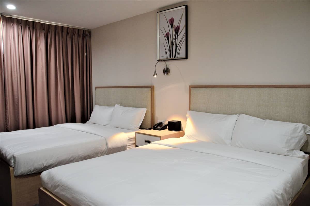 A hotel room with two beds, a nightstand with a phone, and a wall-mounted lamp.