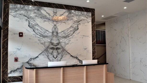A reception desk with a marble wall and a modern design. - Lic Plaza Hotel (Long Island City)