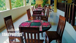 A restaurant with a long table and chairs, a view of greenery outside, and a hand-washing station. - Blue Magpie Lodge (Kalawana)