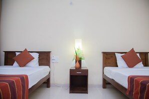 A hotel room with two single beds, each with a brown pillow and a red-striped blanket. A nightstand with a potted plant and a lamp is between the beds. - Blue Magpie Lodge (Kalawana)