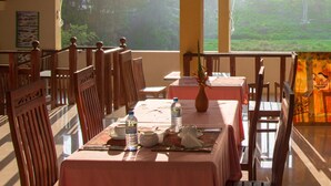 A restaurant with wooden furniture and large windows offering a view of a lush garden. - Blue Magpie Lodge (Kalawana)