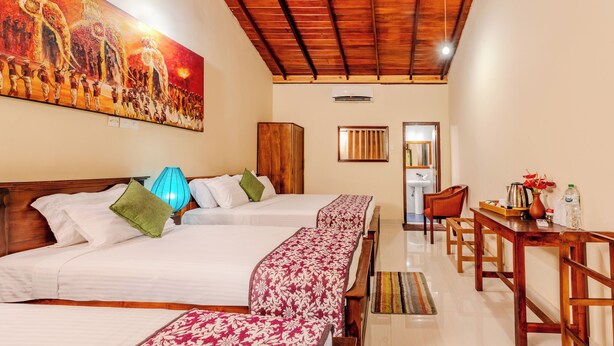 A hotel room with three beds, a wooden ceiling, a painting on the wall, a table with chairs, and a window. - Blue Magpie Lodge (Kalawana)