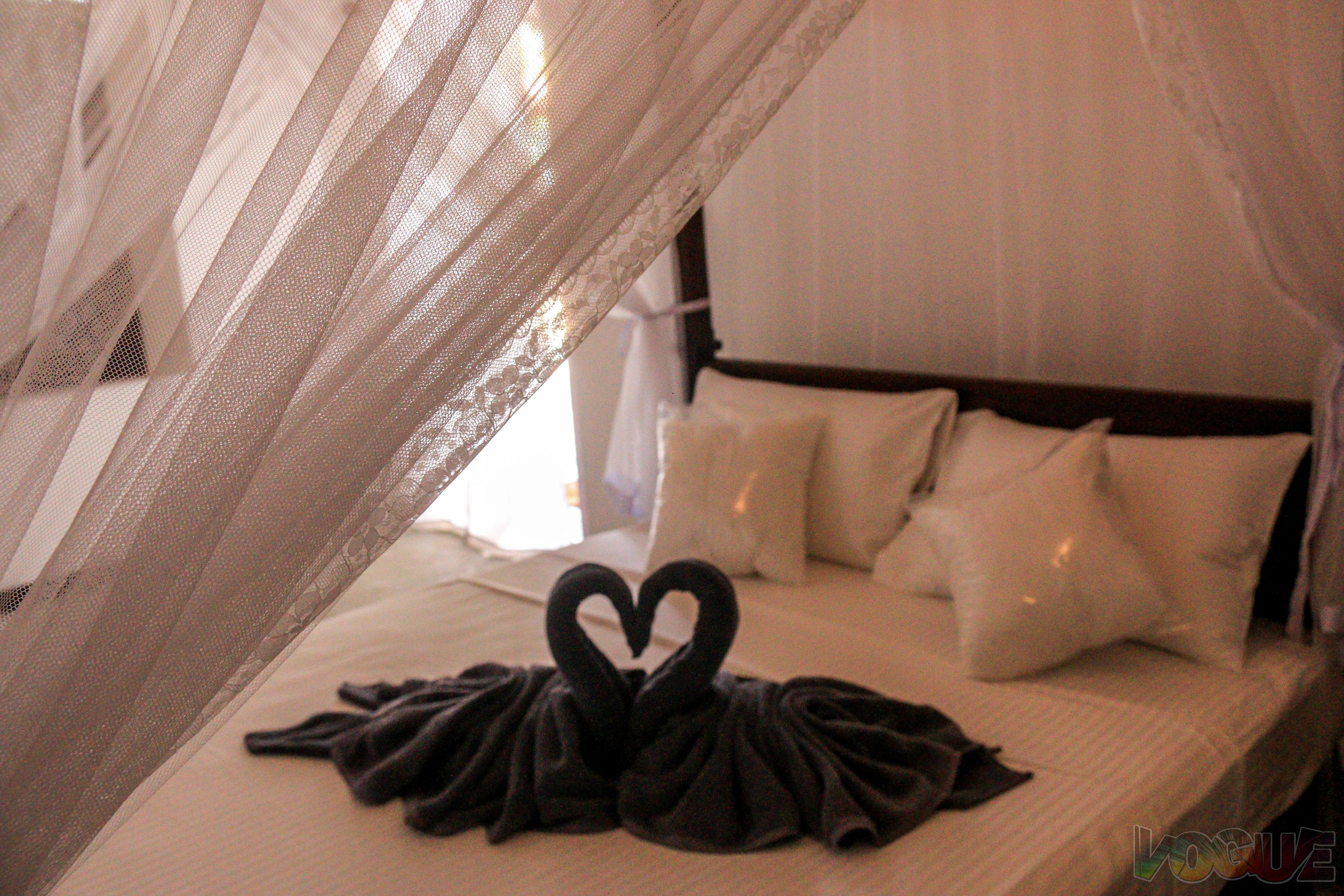A bed with white linens, a canopy, and a towel arranged in a heart shape.