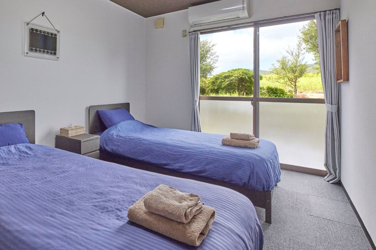 A hotel room with two beds, a small window, and a view of greenery outside.