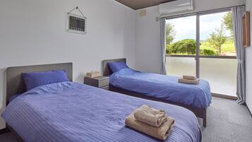 A hotel room with two beds, a small window, and a view of greenery outside.