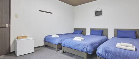 A hotel room with two single beds, a small white refrigerator, and a wall-mounted light fixture.