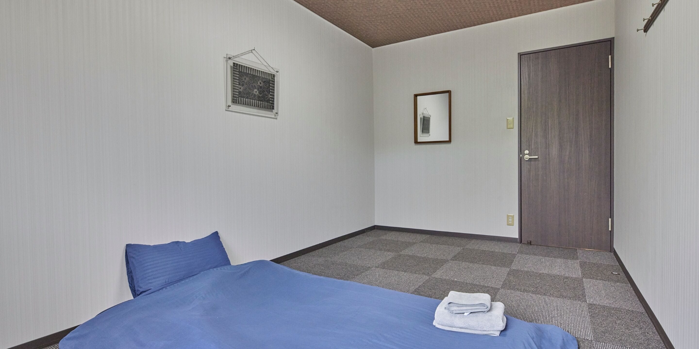 Ein Hotelzimmer mit einem Bett, einem kleinen Fenster, einer Tür und einem gerahmten Bild an der Wand.