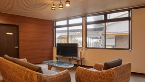 Quarto com móveis de vime, mesa de vidro, televisão de tela plana e amplas janelas com vista para edifícios.