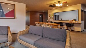 Uma sala de estar moderna com móveis de vime, uma área de jantar com mesa e cadeiras de madeira, e uma cozinha com um espelho grande e bancada.