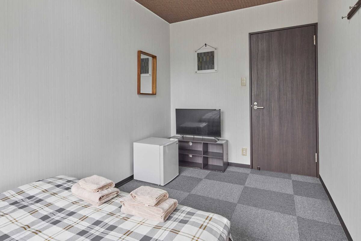 A hotel room with a bed, a TV, a small fridge, and a door.