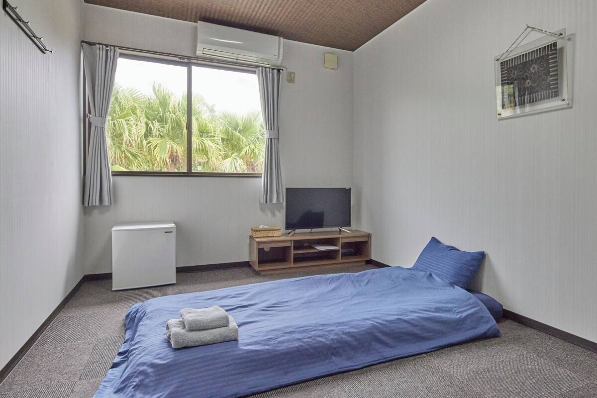 A bedroom with a bed, a TV, a small table, and a window with curtains.