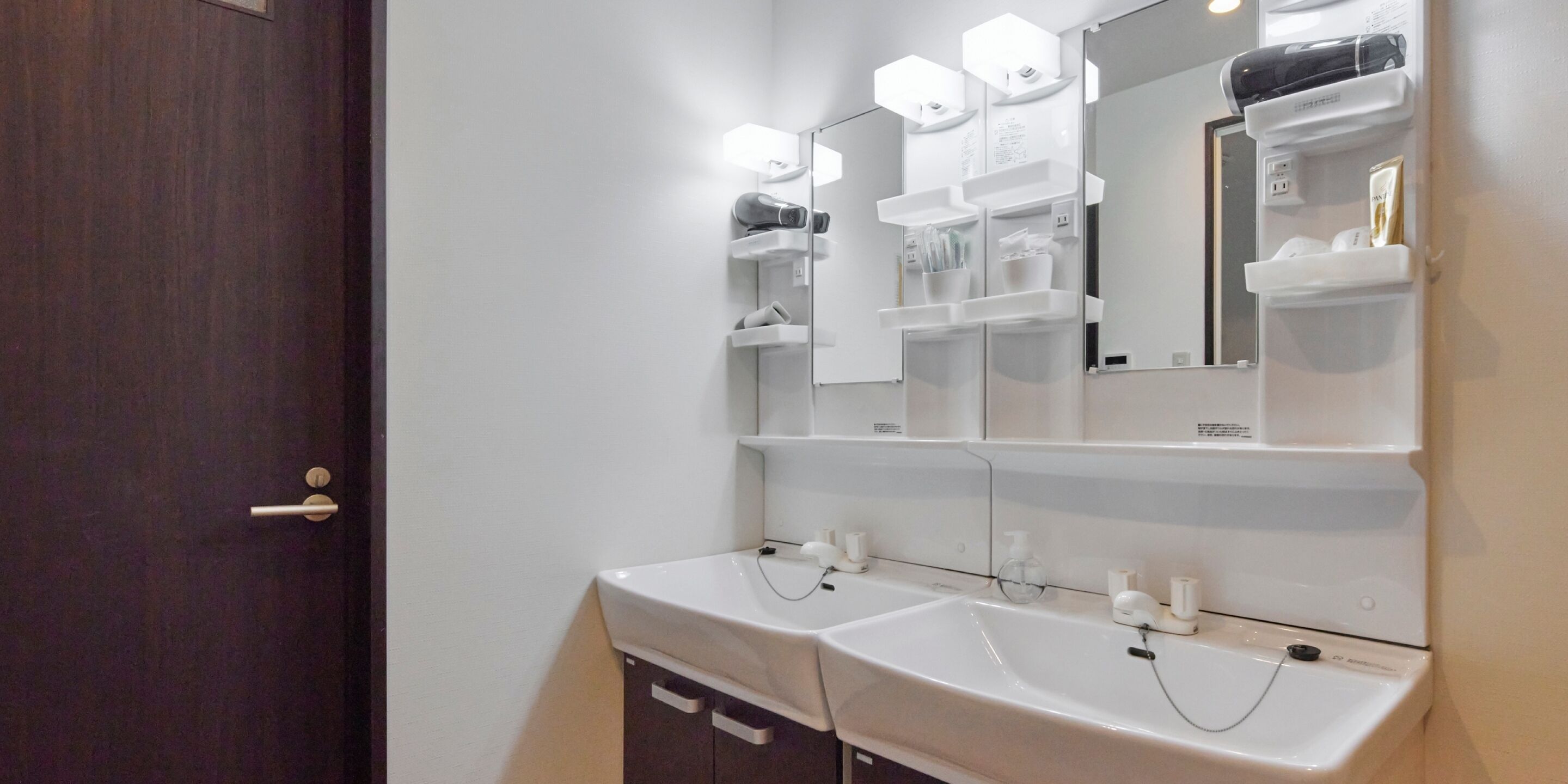 A bathroom with two sinks, a mirror, and shelves with toiletries.