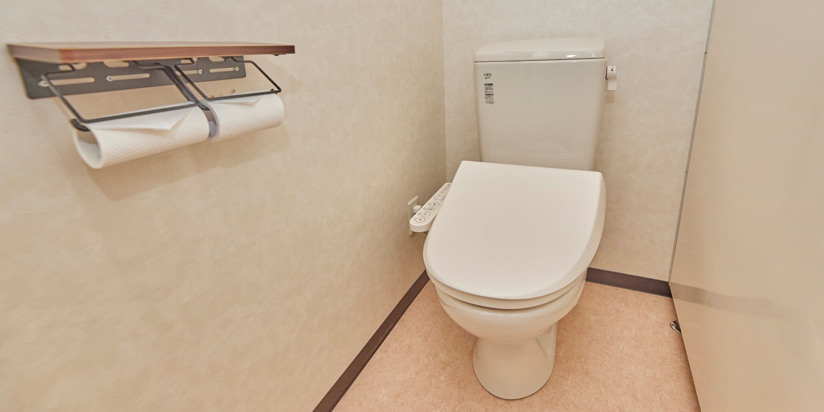 A toilet with a control panel, a toilet paper holder, and a wall-mounted shelf.
