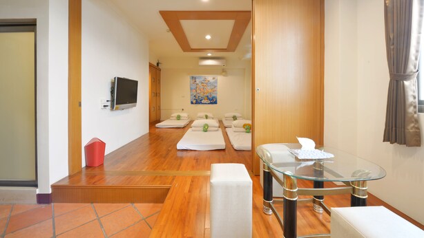 A hotel room with a wooden floor, a glass table, a TV, and a massage table with pillows. - PHSea Inn (Magong)