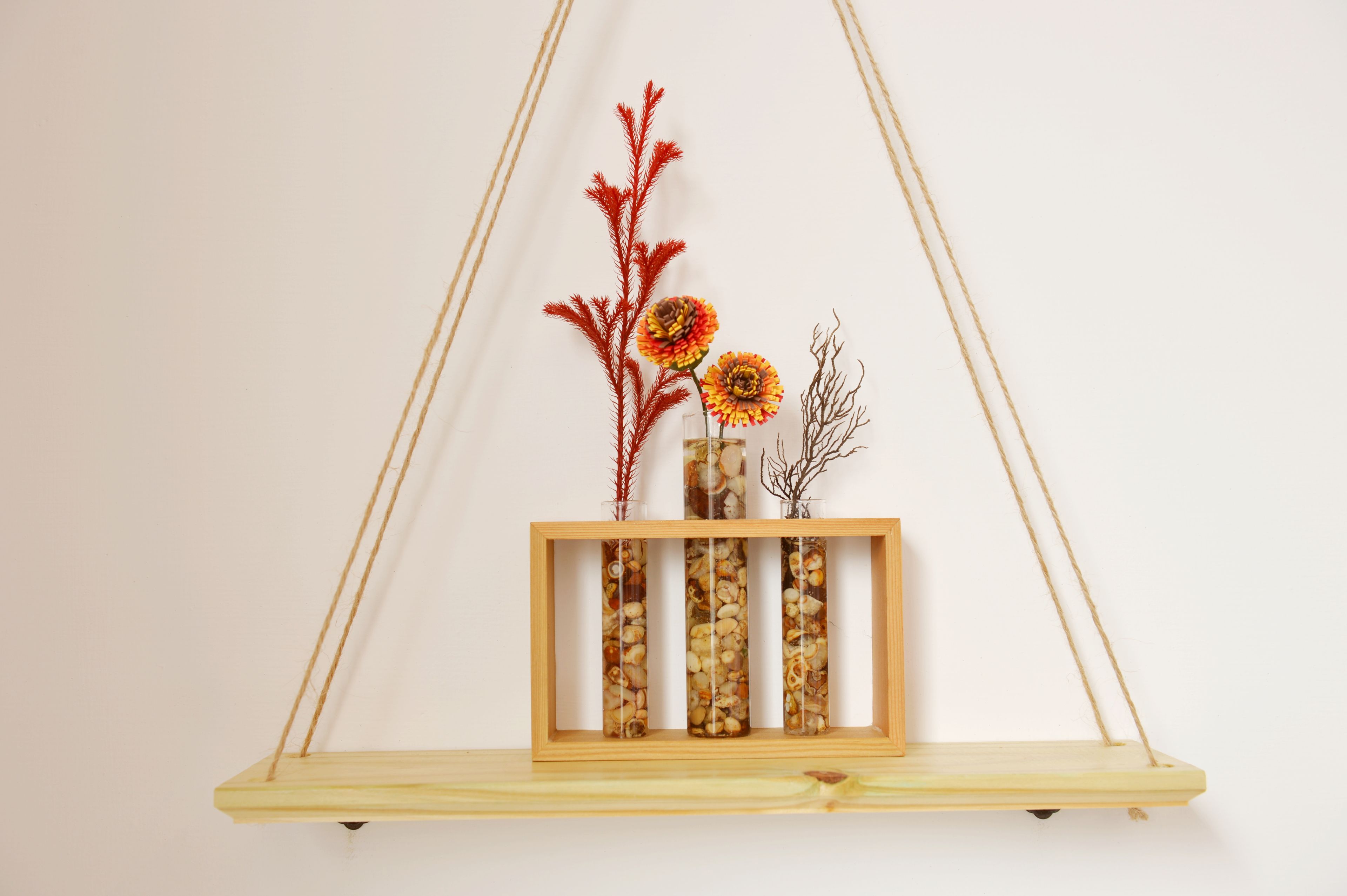A wooden shelf with three glass vases containing dried flowers and shells, suspended by ropes.