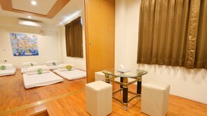 A hotel room with a wooden floor, a glass table with two chairs, a sofa, and a bed with white linens. - PHSea Inn (Magong)