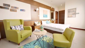 A hotel room with a bed, two green armchairs, a small table, and a decorative wall with artwork. - PHSea Inn (Magong)