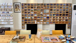 A room with a wall of postcards, a wooden table with various items, and a chair. - PHSea Inn (Magong)