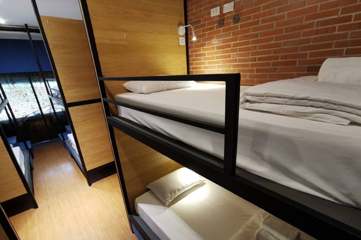 Ein Schlafraum mit Etagenbetten, Holzboden, Backsteinwand und einem kleinen Fenster.