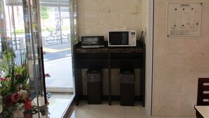 A reception area with a glass door, a microwave, trash bins, and a wall-mounted emergency evacuation plan. - Toyoko Inn Akabane Station Higashi (Tokyo)