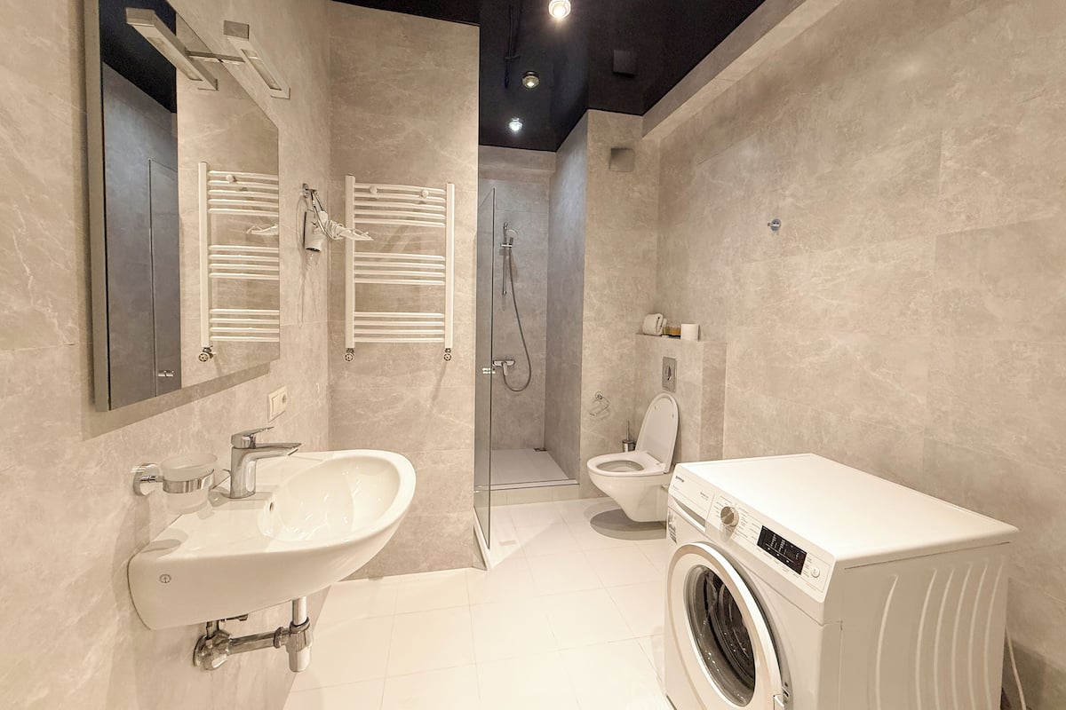 Ein modernes Badezimmer mit Waschbecken, Spiegel, Handtuchhalter, Dusche, Toilette und einer Waschmaschine.