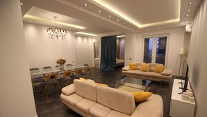 A modern living room with a beige sofa, a glass coffee table, and a dining area with chairs and a table. - Superior Apartments (Tbilisi)