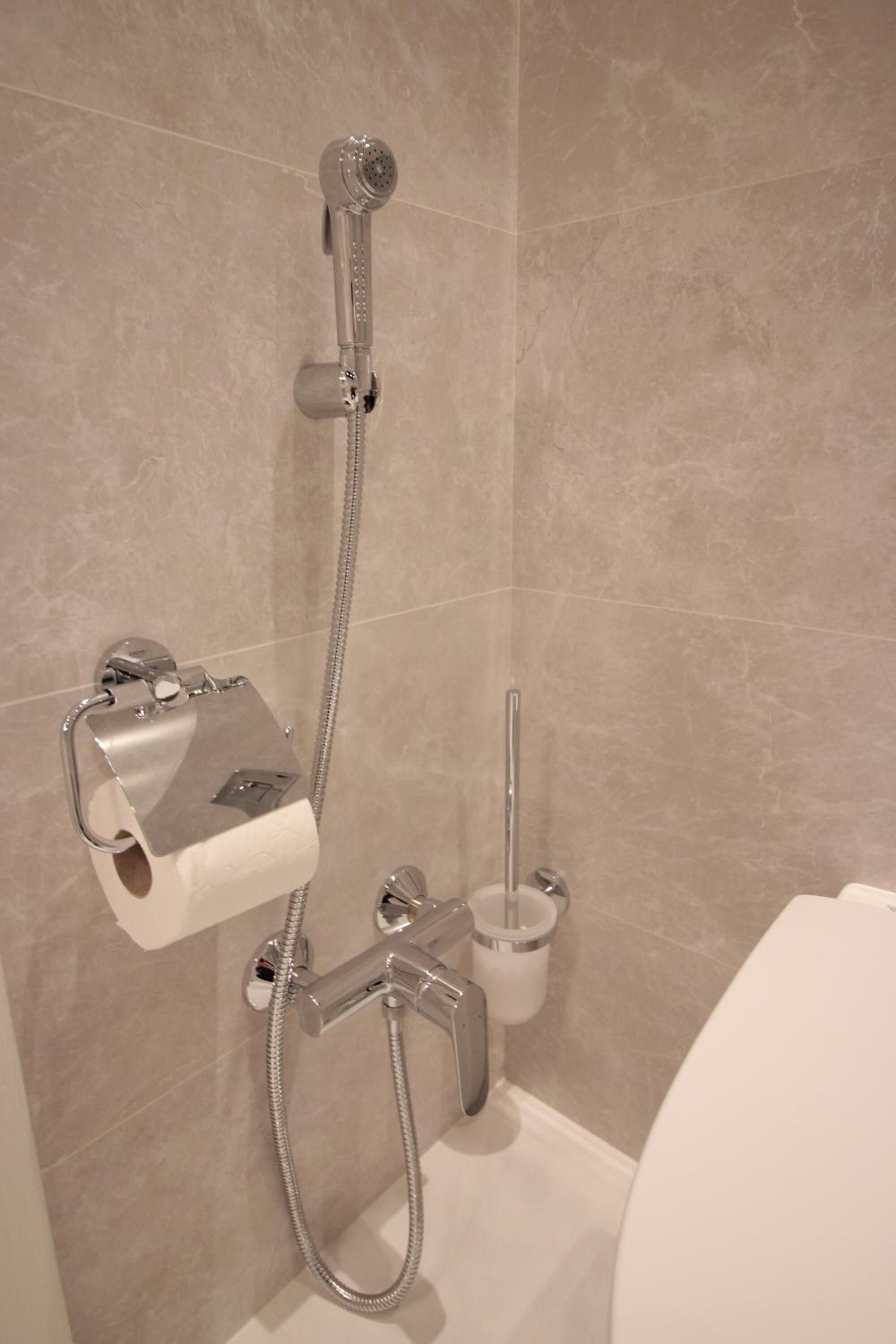 A bathroom with a shower, toilet paper holder, and a toilet.